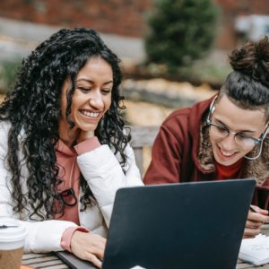 two college students smiling while they look at a laptop computer